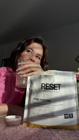 Picture of Reset health Pure Protein and Marianna holding a glass of her protein shake.